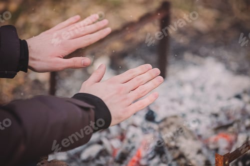 Preview: Traveler Warming His Hands By The Campfire Outdoors. Tea Or Coffee In Aluminum Mug On Background