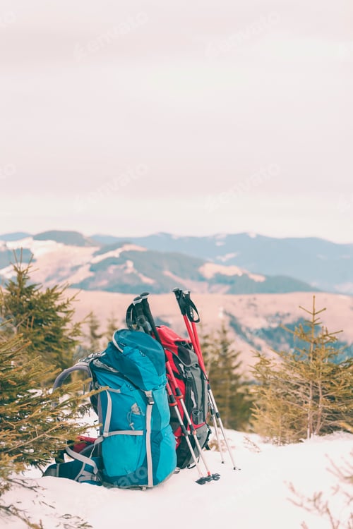 Preview: Two Backpacks In The Background Of Snow-Capped Mountains And Blue Sky. A Backpack On The Snow