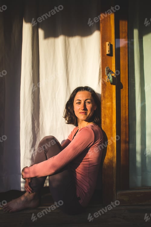 Preview: Attractive Woman Is Sitting Near The Door On The Porch Of A Cozy Wooden House At Sunset. Smiling