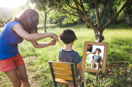 Visualização: Uma mulher corta o cabelo de uma criança no quintal da casa, a mãe corta o cabelo do filho perto da casa