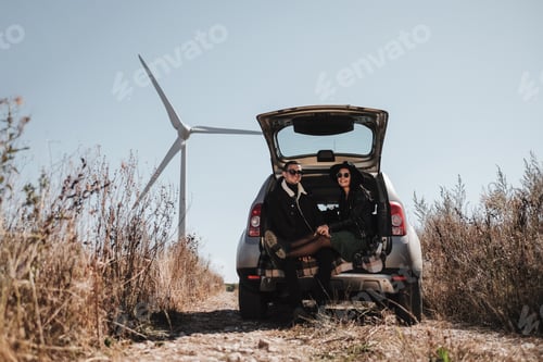 Preview: Happy Traveling Couple Enjoying A Car Trip Sitting In Trunk On The Field Road With Electric Wind
