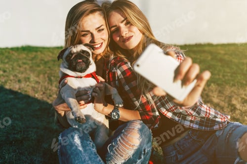 Preview: Two Beautiful Smiling Sisters Twins And Dog Pug Sitting On Green Grass In The Summer Park