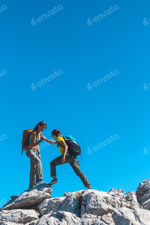 Preview: A Woman Helps Her Friend Climb A Stone. Helping Hand. Two Girls With Backpacks Travel Together.