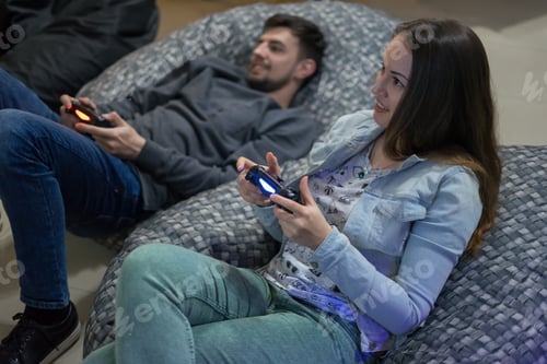Preview: Portrait Of Happy Couple Friends Playing Video Games With Joystick Sitting On Bean Bag Chair. They