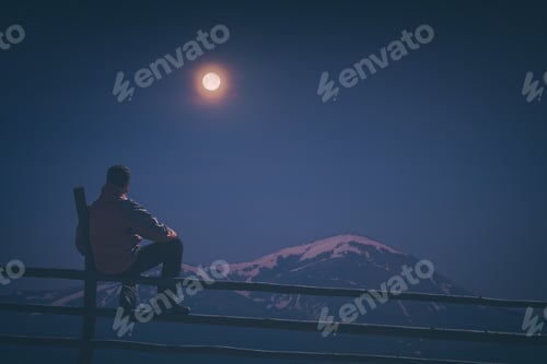 Preview: A Hiker Sitting On A Wooden Fence And Enjoy Rising Of Full Moon Above The High Mountain Covered