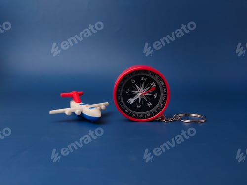 Preview: A small toy airplane with red wings sits next to a red compass keychain against a solid blue backdro