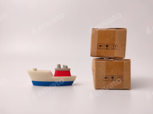 Preview: A small toy cargo ship with a red cabin sits next to two stacked miniature cardboard boxes