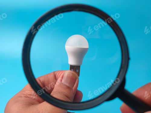 Preview: A small USB LED light bulb held in a hand is focused on through a magnifying glass against blue