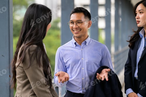 Preview: Smiling asian businessman communicating with female colleagues outdoors