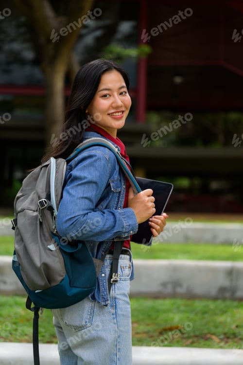 Preview: Young Asian female student smiling on campus holding tablet