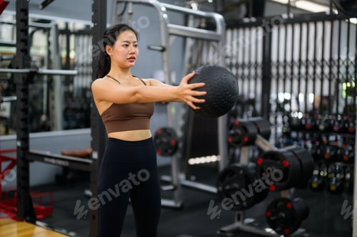 Preview: Young woman training with medicine ball in gym