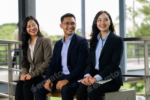 Preview: Smiling diverse business people sitting outdoors discussing work