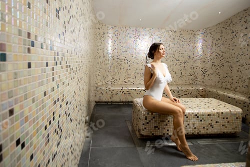 Preview: Woman relaxes in spa room with tiled walls and seating during wellness visit