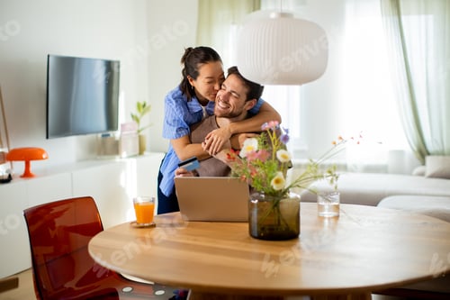 Preview: Couple enjoying time together at home while working on a laptop in the morning