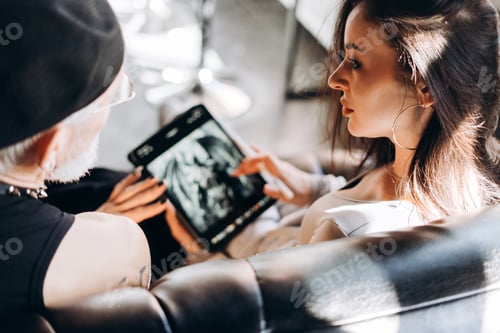 Preview: Tattoo artist consulting client choosing design with tablet