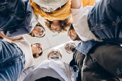 Preview: Diverse group of people standing in huddle looking down