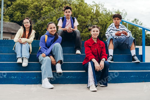 Preview: Portrait of diverse teenage friends sitting together on skatepark steps