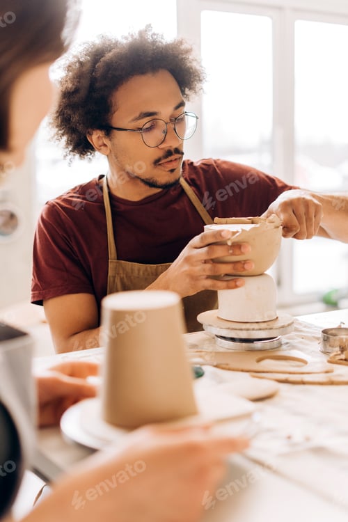 Preview: African American male ceramic artist sculpting clay bowl in workshop