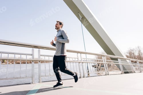 Preview: Side view of athletic man running on bridge during outdoor training