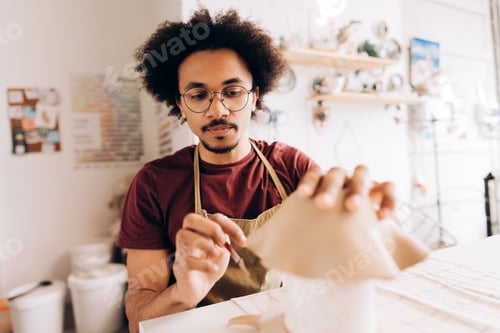 Preview: Young African American man creating ceramic pottery in a home workshop