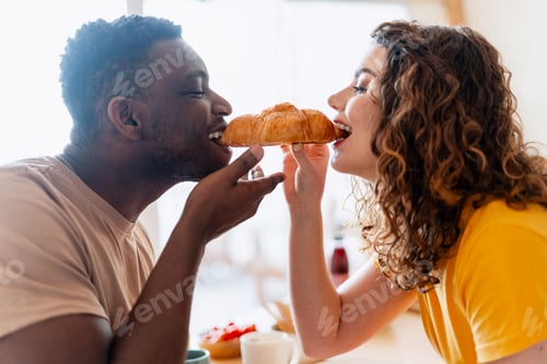 Preview: Interracial couple sharing croissant during breakfast meal