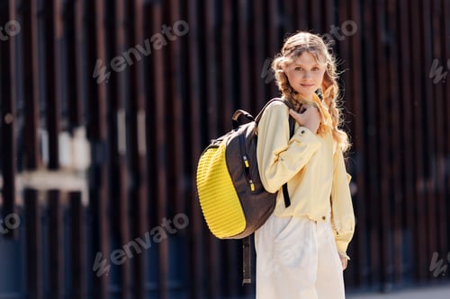 Preview: Portrait of beautiful teen girl with backpack looking at camera standing on the street