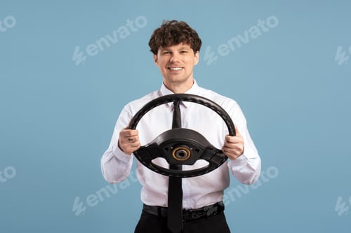 Preview: Smiling businessman holding steering wheel isolated on blue background