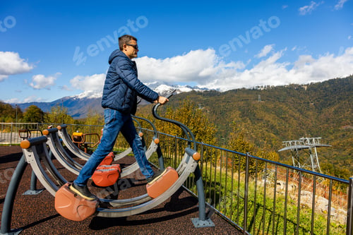 Preview: Man exercises on outdoor fitness equipment with a mountain view