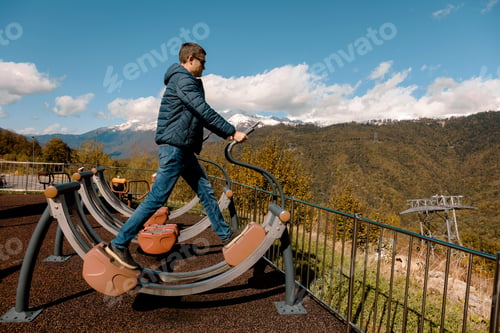 Preview: Man uses outdoor exercise machine on mountain with snow-capped peaks