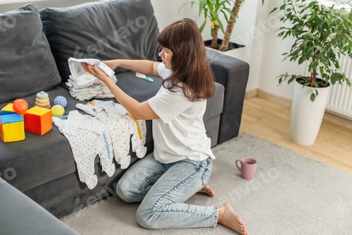 Preview: Mother folding baby clothes on sofa at home