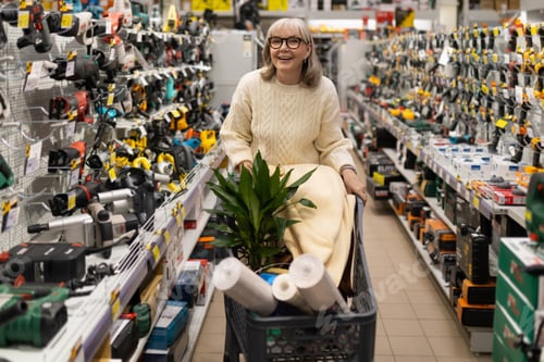 Preview: Woman pushing a shopping cart with plant and building materials in tool aisle