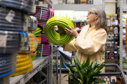 Preview: Senior woman shopping for a garden hose and plants in a large retail store