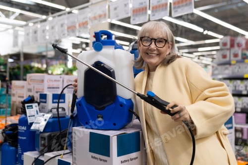Preview: Senior woman at hardware store choosing a battery powered garden sprayer