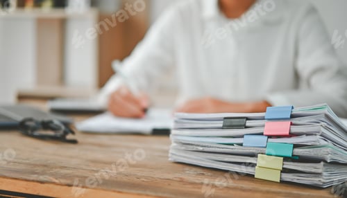 Preview: A person is sitting at a desk with a stack of papers in front of them
