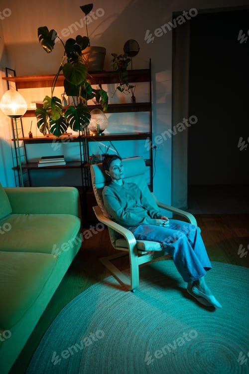 Preview: Unmotivated tired woman sitting in living room in color rgb light feeling fatigue and apathy.