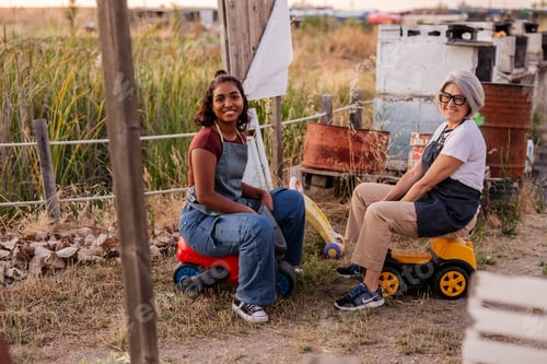Preview: Two women farm workers sitting on toy vehicles smiling