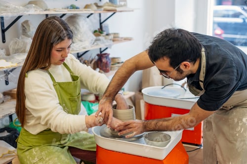 Preview: Pottery instructor guiding student hands shaping clay on wheel