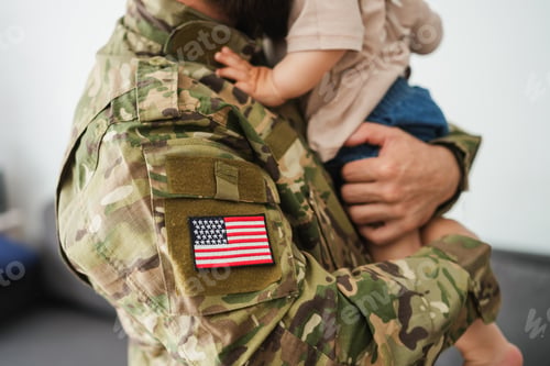 Preview: Male american soldier in military uniform hugs his little son at home