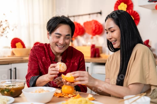 Preview: Asian couple celebrating Lunar New Year, eating orange together at table.