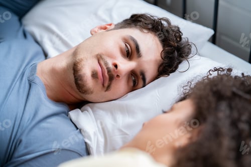 Preview: Latino young couple lying down together on bed in cozy bedroom at home.