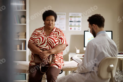 Preview: Black Middle Aged Woman Waiting While Doctor Reviewing Chart