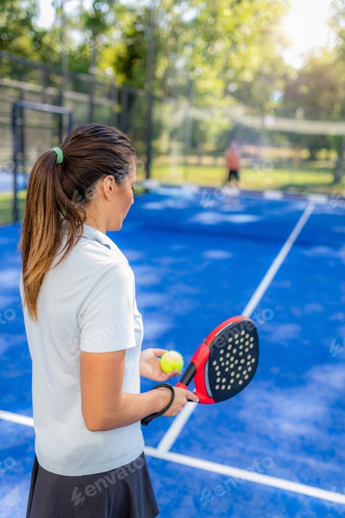 Preview: Woman holding padel racket and ball preparing to serve on outdoor court, calm moment before next ral