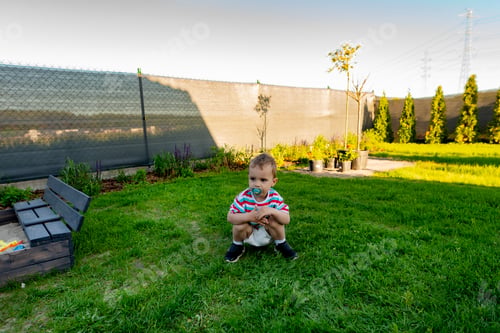 Preview: Little boy crouching in garden with pacifier
