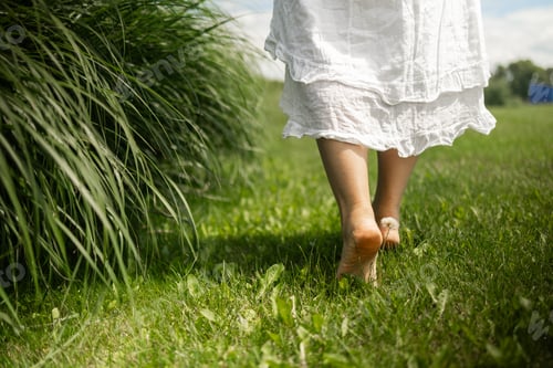 Preview: Woman in white dress walking barefoot on green grass outdoors, close up. Space for text