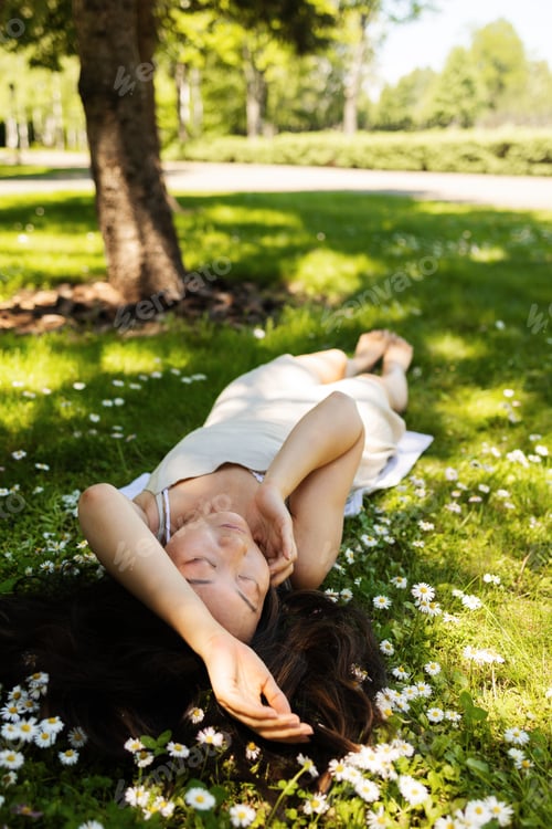 Preview: Young Asian woman lying down in the green grass with chamomile, enjoying nature in spring.