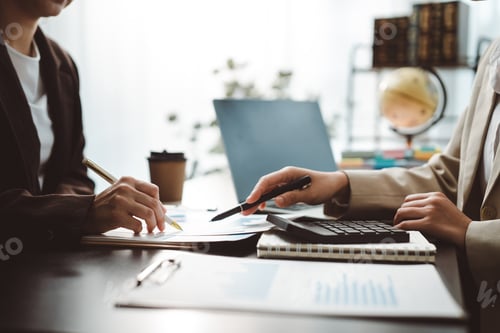 Preview: Business professionals gathered around a desk, analyzing financial reports and charts, using calcula