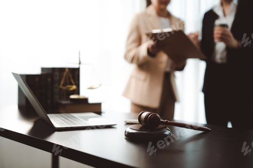 Preview: Legal professionals discussing client case while gavel and laptop rest on a dark office desk, repres