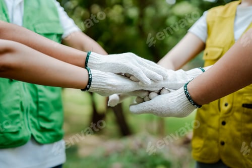 Preview: Volunteers wearing gloves stack hands in a circle outdoors, symbolizing teamwork, unity and commitme
