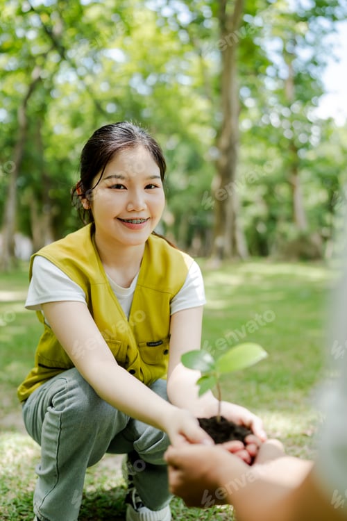 Preview: Young asian girl receiving a small green plant with soil from another person, symbolizing care for t