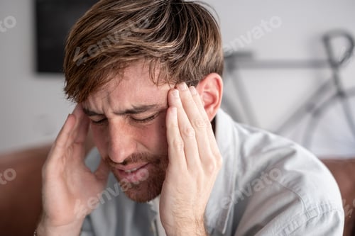 Preview: Young Man Holding Head in Pain With Migraine, Stress and Tension at Home